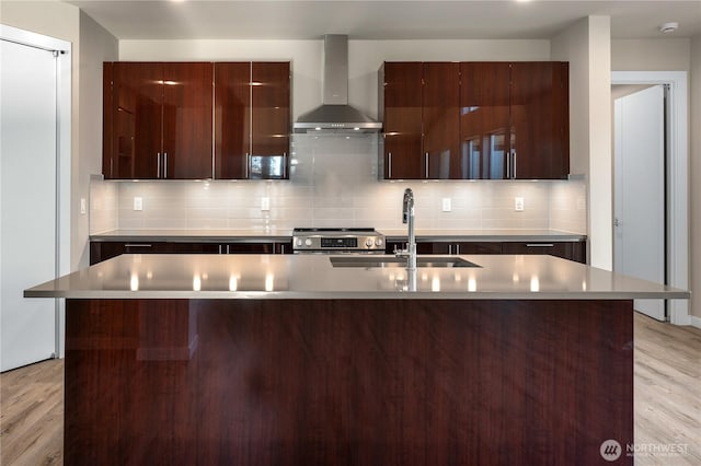 kitchen featuring wall chimney exhaust hood, modern cabinets, stainless steel range with electric cooktop, light wood-style floors, and a sink