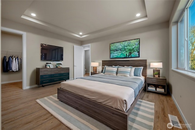 bedroom with light wood-type flooring, baseboards, a spacious closet, and a tray ceiling