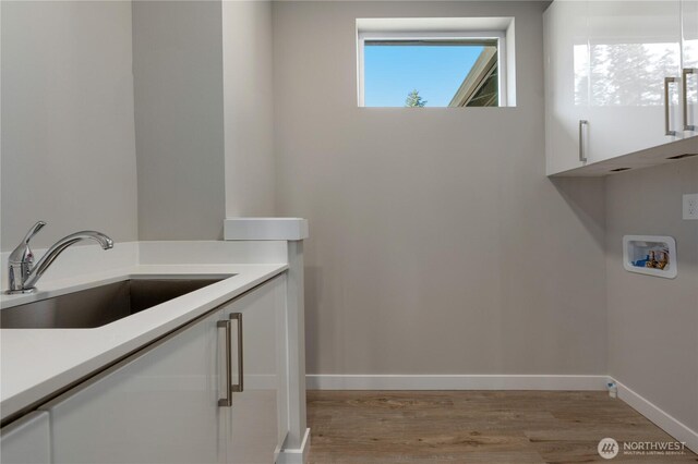 washroom with washer hookup, cabinet space, light wood-style flooring, a sink, and baseboards