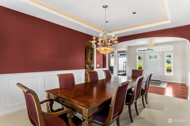 dining space with light carpet, a tray ceiling, and an inviting chandelier