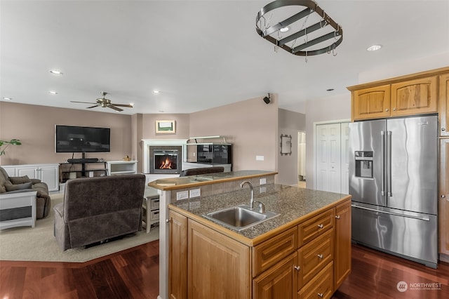 kitchen featuring dark wood-type flooring, stainless steel fridge with ice dispenser, an island with sink, and sink