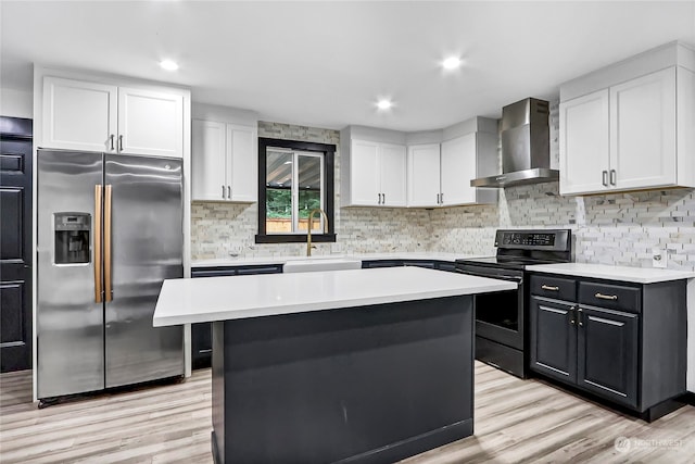 kitchen with wall chimney range hood, appliances with stainless steel finishes, sink, light wood-type flooring, and a kitchen island