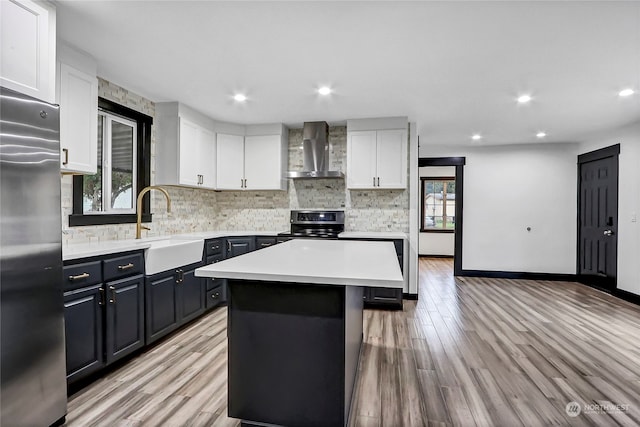 kitchen featuring a kitchen island, wall chimney range hood, stainless steel appliances, light wood-type flooring, and white cabinetry