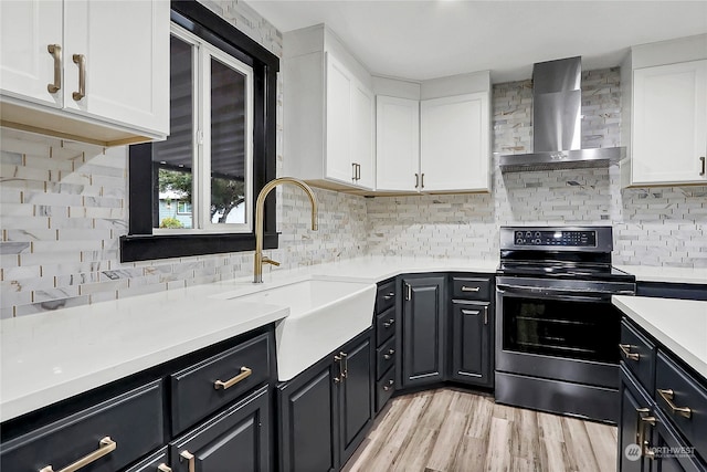 kitchen featuring decorative backsplash, wall chimney exhaust hood, stainless steel range, sink, and white cabinets