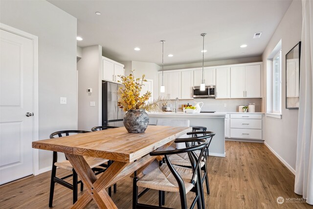 kitchen with appliances with stainless steel finishes, hanging light fixtures, white cabinetry, and light hardwood / wood-style floors