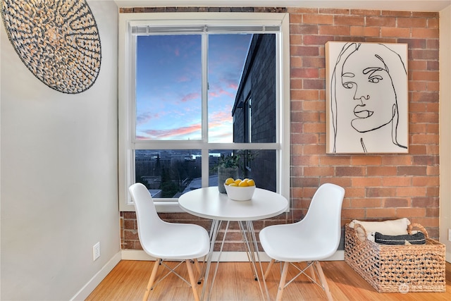 dining space with hardwood / wood-style floors and brick wall