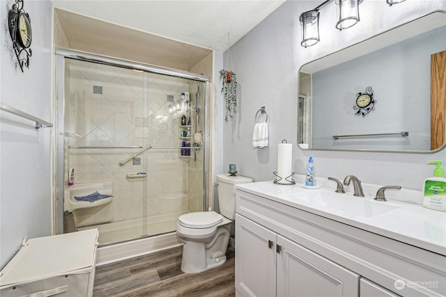 bathroom featuring a shower with door, vanity, wood-type flooring, and toilet