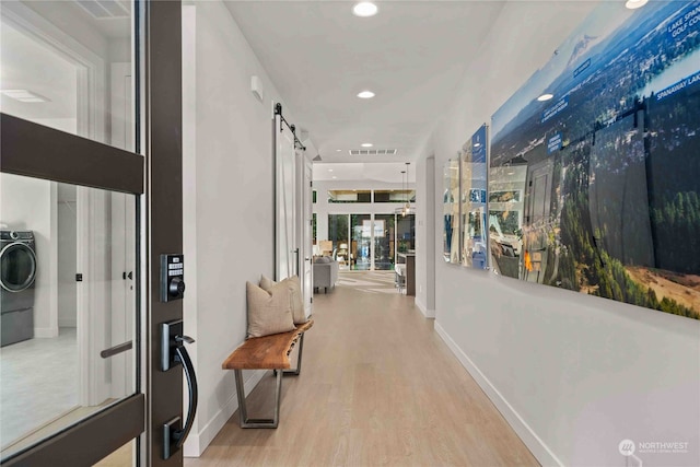 corridor with a barn door, light hardwood / wood-style floors, and washer / clothes dryer