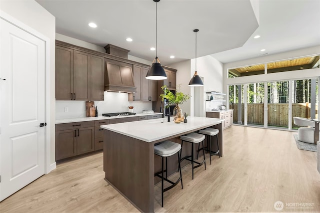 6361LOT257 Great Glen Rd SW, Port Orchard, WA 98367 - kitchen featuring gas cooktop, light countertops, a kitchen island with sink, premium range hood, and light wood-type flooring