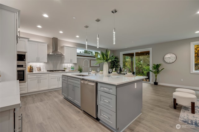 kitchen with stainless steel appliances, wall chimney range hood, pendant lighting, sink, and a kitchen island with sink