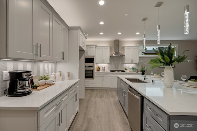 kitchen featuring appliances with stainless steel finishes, hanging light fixtures, sink, light hardwood / wood-style floors, and wall chimney exhaust hood