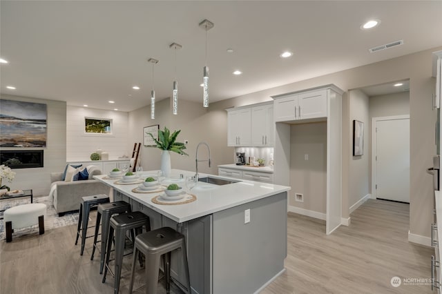 kitchen featuring a center island with sink, sink, a kitchen breakfast bar, hanging light fixtures, and white cabinets