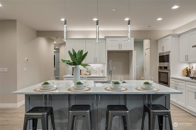 kitchen with a kitchen island with sink, appliances with stainless steel finishes, decorative light fixtures, and a breakfast bar