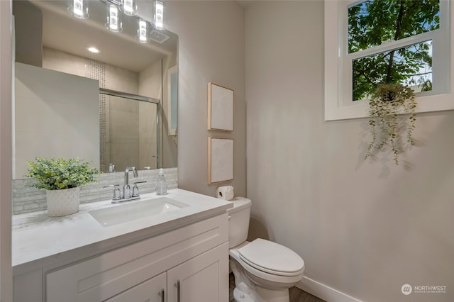 bathroom with vanity, toilet, a shower with door, and backsplash