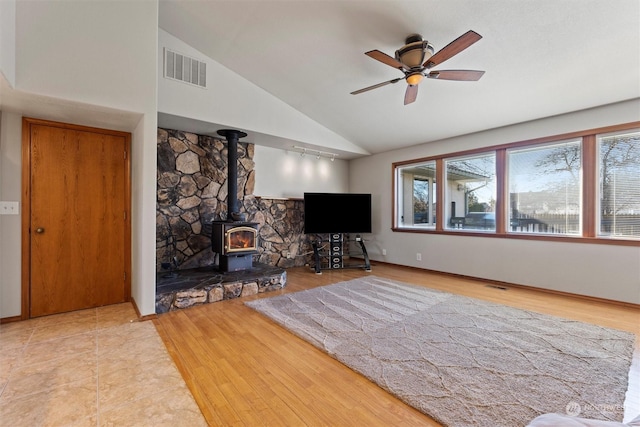 unfurnished living room featuring vaulted ceiling, a wood stove, ceiling fan, and light wood-type flooring