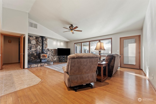 living room featuring vaulted ceiling, ceiling fan, light hardwood / wood-style floors, and a wood stove