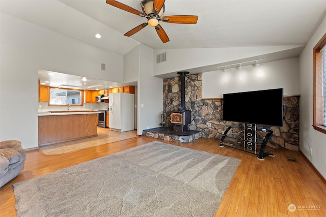 living room with rail lighting, lofted ceiling, a wood stove, ceiling fan, and light wood-type flooring