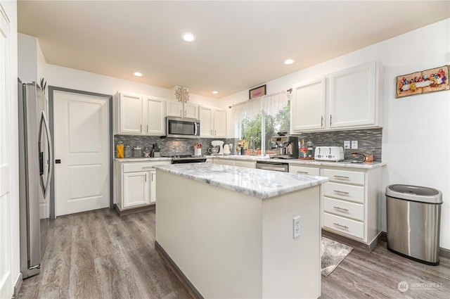 kitchen featuring appliances with stainless steel finishes, wood-type flooring, a center island, white cabinets, and decorative backsplash