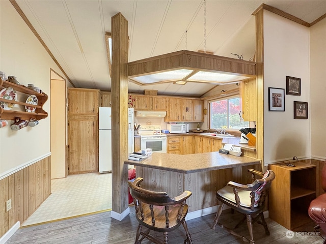 kitchen with kitchen peninsula, wood-type flooring, wood walls, sink, and white appliances