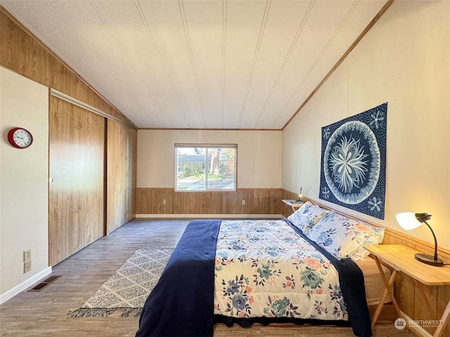 bedroom featuring lofted ceiling, hardwood / wood-style floors, ornamental molding, and wood walls