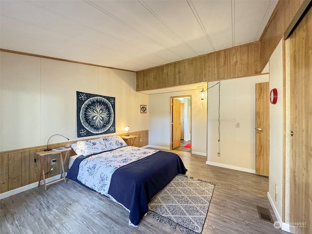 bedroom with crown molding, wood walls, and hardwood / wood-style flooring