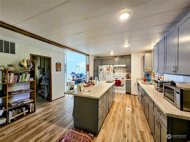 kitchen featuring light stone counters, a kitchen island, light wood-type flooring, sink, and white appliances