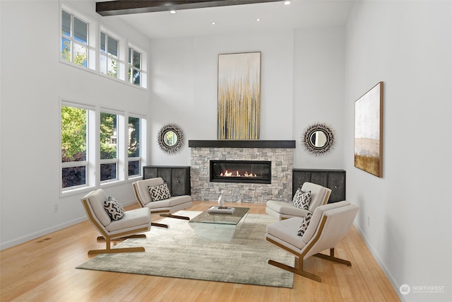 sitting room with beamed ceiling, a high ceiling, light hardwood / wood-style flooring, and a stone fireplace