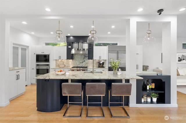 kitchen featuring white cabinets, built in appliances, light hardwood / wood-style flooring, and wall chimney exhaust hood