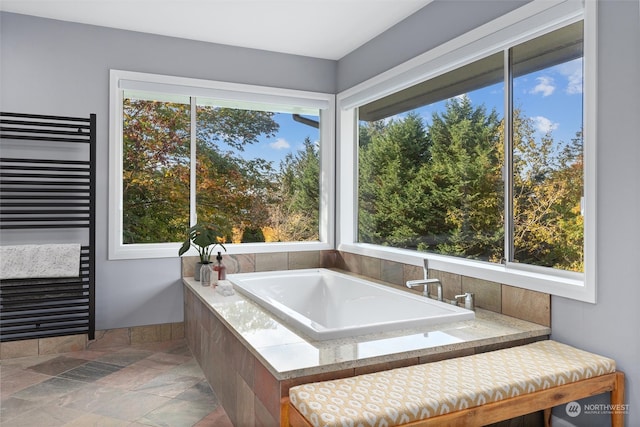 bathroom featuring a wealth of natural light, radiator heating unit, and a relaxing tiled tub