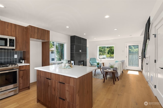 kitchen with backsplash, appliances with stainless steel finishes, light hardwood / wood-style flooring, and a tile fireplace