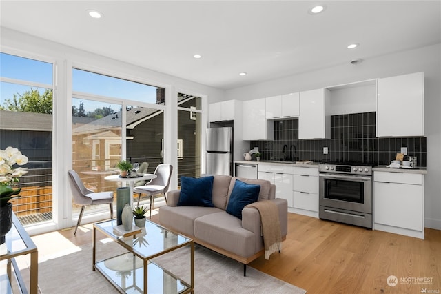 kitchen with white cabinets, backsplash, appliances with stainless steel finishes, light wood-type flooring, and sink