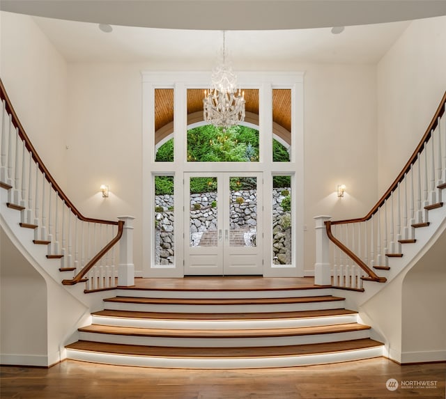 entryway with french doors, a towering ceiling, a notable chandelier, and wood-type flooring