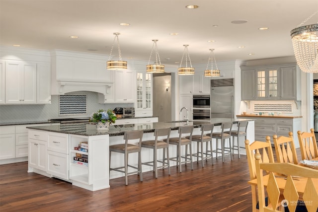 kitchen with appliances with stainless steel finishes, a spacious island, dark hardwood / wood-style flooring, dark stone counters, and pendant lighting