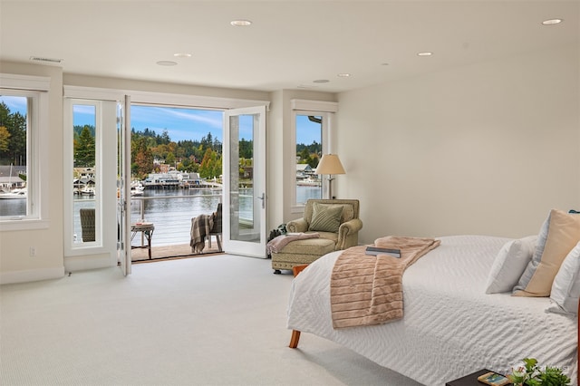 bedroom featuring carpet, a water view, multiple windows, and access to outside