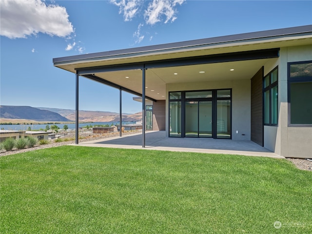 rear view of house with a patio area, a water and mountain view, and a lawn