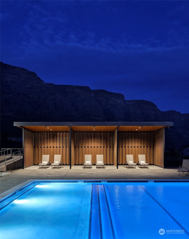 pool at twilight featuring a mountain view and a patio area