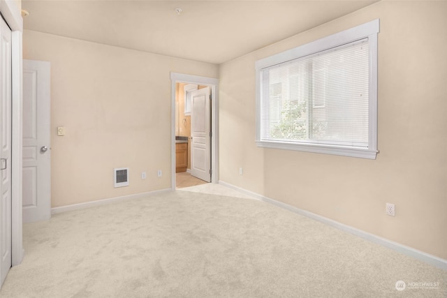 unfurnished bedroom with connected bathroom and light colored carpet