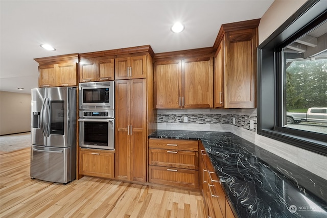 kitchen featuring decorative backsplash, appliances with stainless steel finishes, light hardwood / wood-style flooring, and dark stone counters