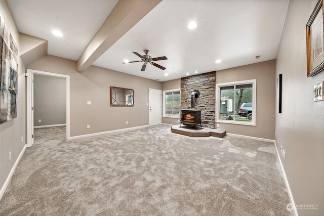 unfurnished living room with carpet flooring, ceiling fan, a wood stove, and beamed ceiling