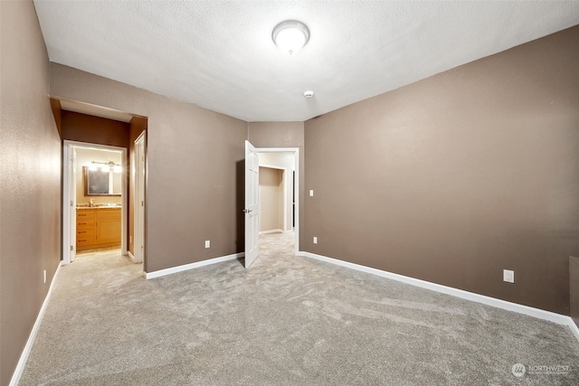 unfurnished bedroom with a textured ceiling, light colored carpet, and ensuite bath