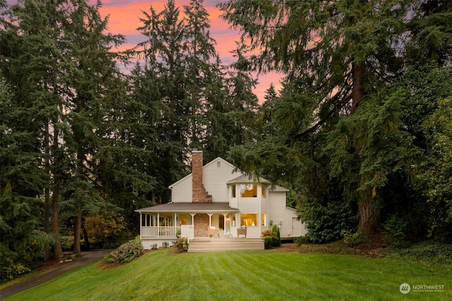 back house at dusk with covered porch and a yard