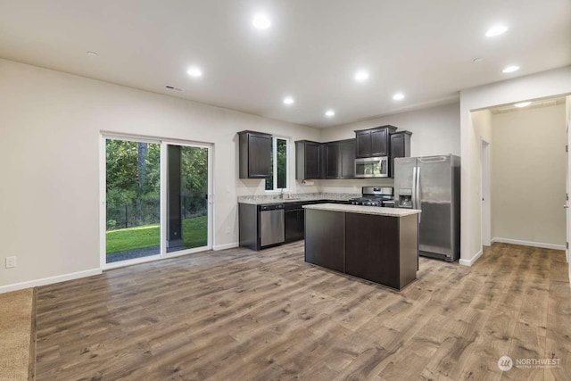 kitchen featuring light stone counters, appliances with stainless steel finishes, a kitchen island, and light hardwood / wood-style flooring