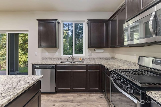 kitchen with dark brown cabinetry, stainless steel appliances, light stone countertops, and sink