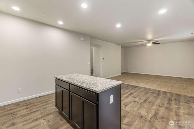 kitchen with light stone counters, dark brown cabinets, light hardwood / wood-style flooring, a kitchen island, and ceiling fan