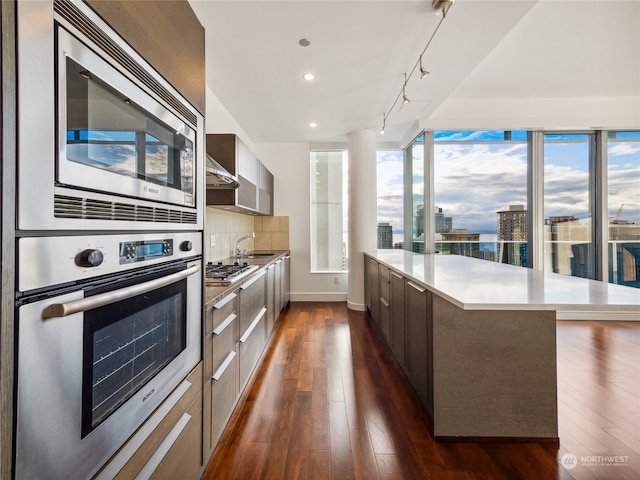 kitchen featuring sink, a center island, stainless steel appliances, dark wood-type flooring, and decorative backsplash