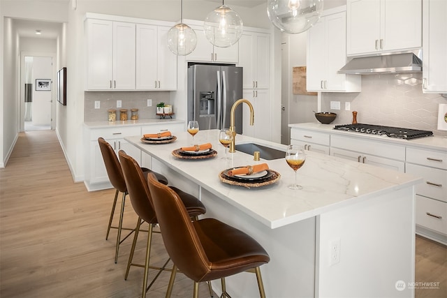 kitchen with light wood-type flooring, appliances with stainless steel finishes, a center island with sink, and sink