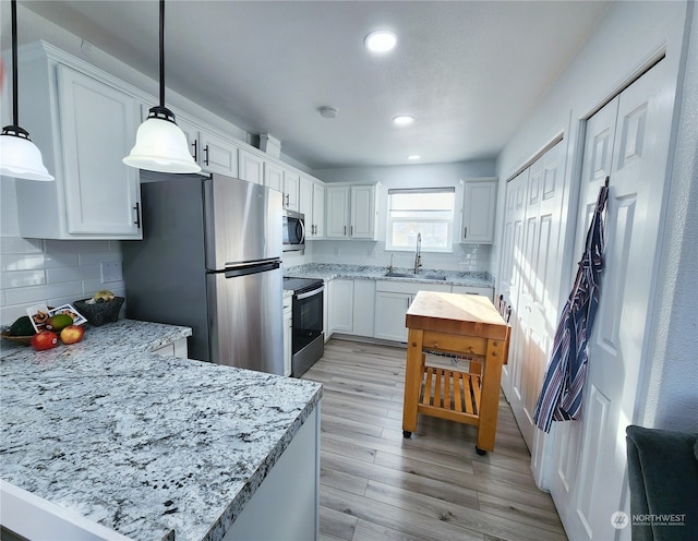 kitchen with appliances with stainless steel finishes, pendant lighting, decorative backsplash, white cabinets, and light hardwood / wood-style flooring