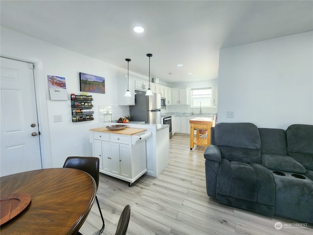 kitchen featuring stainless steel appliances, hanging light fixtures, sink, white cabinets, and light hardwood / wood-style flooring