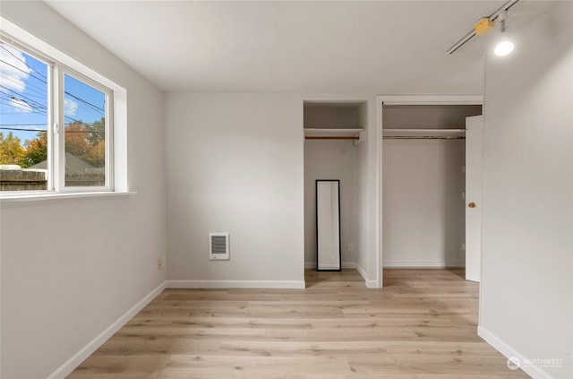 unfurnished bedroom with light hardwood / wood-style flooring, two closets, and heating unit