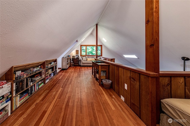 bonus room featuring light hardwood / wood-style flooring, wood walls, a textured ceiling, and lofted ceiling